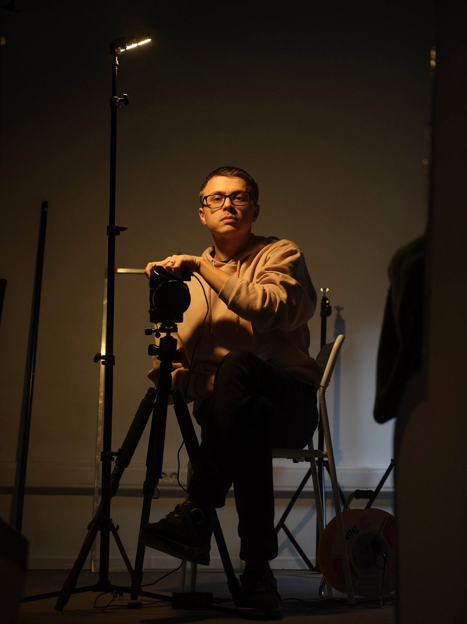 Gleb Kalinin seated in a studio beside a camera and lighting equipment